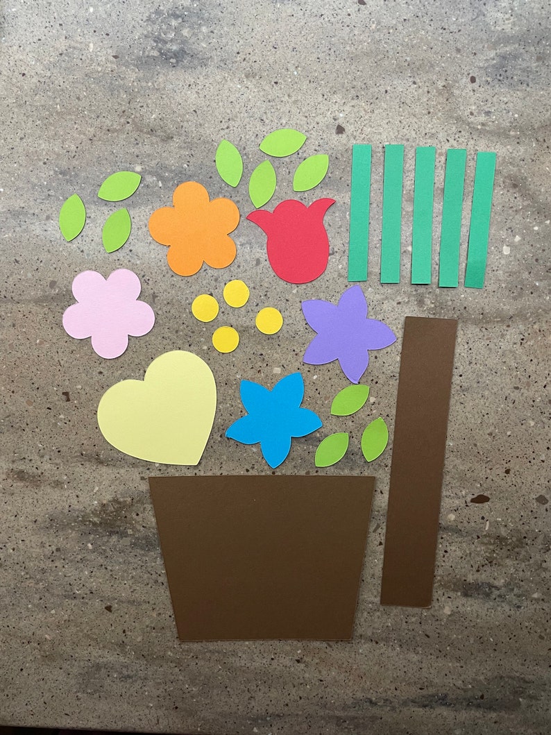 May include: A craft project with paper cutouts of a flower pot, flowers, leaves, and stems. The pieces are in various colors, including green, yellow, orange, red, pink, purple, and brown.