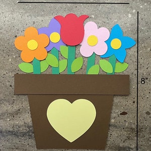 May include: A brown paper flower pot with a yellow heart cutout, holding five paper flowers. The flowers are red, orange, pink, purple, and blue. The pot is 8 inches tall and 6.5 inches wide.