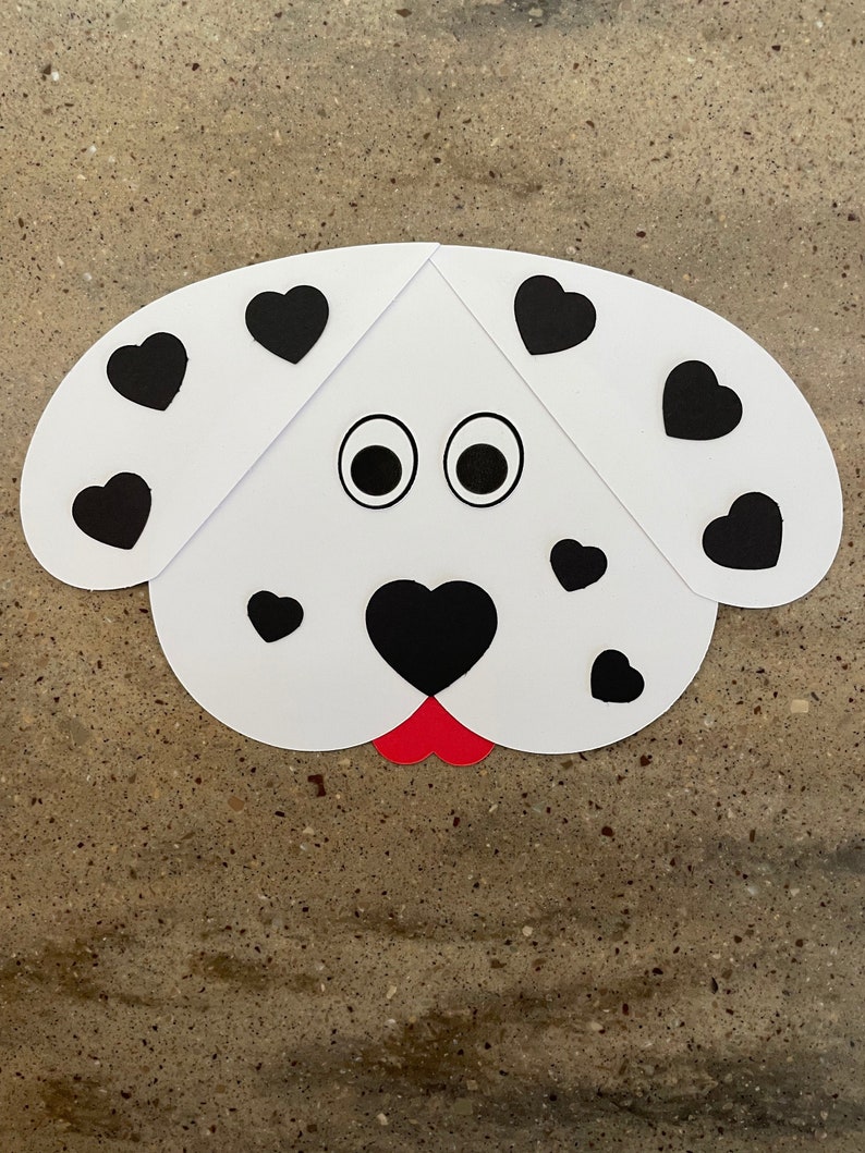 May include: A white paper dalmatian dog craft with black heart-shaped spots and googly eyes. The dog has a red tongue.