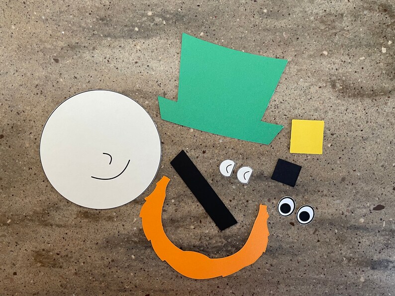 May include: A craft project with paper cutouts for making a leprechaun. The pieces include a white circle for the face, a green hat, a black mustache, orange beard, yellow square, black square, and two white eyes.