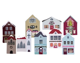 May include: A collection of colorful, illustrated houses with snow-covered roofs. The buildings include a gift shop, a book shop, and a toy shop, with Christmas decorations visible in some windows. The houses are set against a white background.