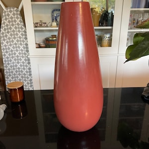 May include: A tall, slender, terracotta-colored ceramic vase with a rounded bottom and a narrow opening. The vase is sitting on a black surface.