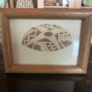 Könnte beinhalten: Ein gerahmter Druck einer braunen und weißen Töpferschale mit geometrischen Mustern. Der Druck ist in einem Holzrahmen mit hellbrauner Oberfläche.