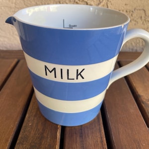 May include: A ceramic measuring cup with a white handle and a spout. The cup features blue and white horizontal stripes and the word "MILK" in black. The cup has a capacity marking near the rim.