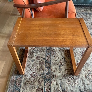 May include: A rectangular wooden coffee table with a light brown finish. The table has a simple, geometric design with angled legs. The table is approximately 30 inches long, 18 inches wide, and 16 inches high.