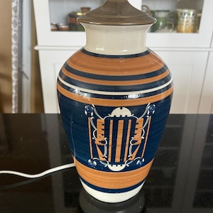 May include: A ceramic table lamp with a blue and brown geometric design. The lamp has a white base and a brass top.