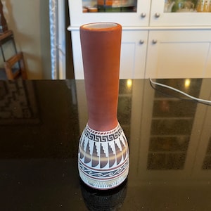 May include: A brown ceramic vase with a white and brown geometric design. The vase has a narrow neck and a wide base.