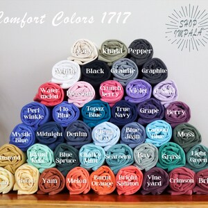 May include: A pyramid of rolled fabric swatches in various colors, including mustard, banana, berry, and seafoam. The fabric swatches are labeled with color names, such as "Topaz Blue", "Midnight Blue", and "Vineyard". The text "Comfort Colors 1717" is at the top of the image.