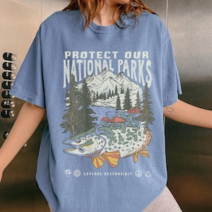 May include: A light blue t-shirt with a graphic print of a mountain scene and a fish. The text "PROTECT OUR NATIONAL PARKS" is printed on the shirt. The text "EXPLORE RESPONSIBLY" is printed below the graphic.