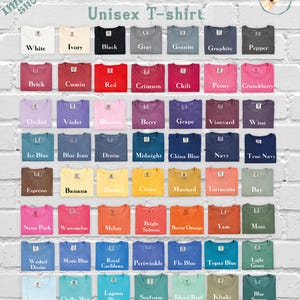 Pode incluir: Uma tabela de cores para camisetas unissex Comfort Colors com 63 camisetas dobradas em v&aacute;rios tons, incluindo branco, preto, vermelho, azul, amarelo, rosa e verde. Cada camiseta est&aacute; rotulada com o nome da cor. O texto diz Impala Shop.