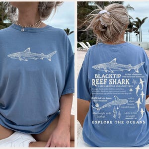 May include: A light blue t-shirt with a white shark graphic on the front. The back of the shirt has a detailed illustration of a Blacktip Reef Shark, scientific details, and the words "Explore the Oceans".