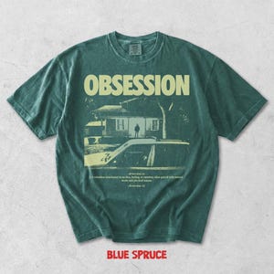 May include: A dark green short-sleeve t-shirt featuring the word OBSESSION in large letters above a graphic of a house and a car. Below the graphic, the text reads: obsession (n) 1. A relentless attachment to an idea, feeling, or emotion.
