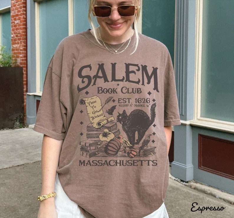 May include: Espresso-colored t-shirt with a graphic design for the Salem Book Club. The design includes a black cat, books, and the text "Time to Get Wicked." The shirt also features the text "EST. 1626" and "Massachusetts."