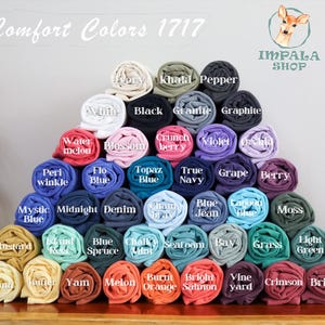 Puede incluir: Una pila piramidal de camisetas Comfort Colors 1717 enrolladas en varios colores, incluyendo marfil, negro, pimienta, blanco, sand&iacute;a, flor, baya crujiente, violeta, orqu&iacute;dea, b&iacute;garo, azul, topacio, marino, uva, baya, azul m&iacute;stico y otros.