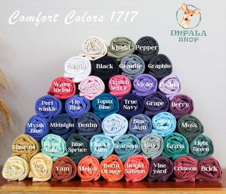 Puede incluir: Una pila piramidal de camisetas Comfort Colors 1717 enrolladas en varios colores, incluyendo marfil, negro, pimienta, blanco, sand&iacute;a, flor, baya crujiente, violeta, orqu&iacute;dea, b&iacute;garo, azul, topacio, marino, uva, baya, azul m&iacute;stico y otros.