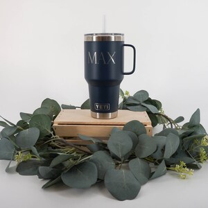May include: A navy blue YETI tumbler with a straw and a handle. The tumbler has the name "MAX" engraved on the side.