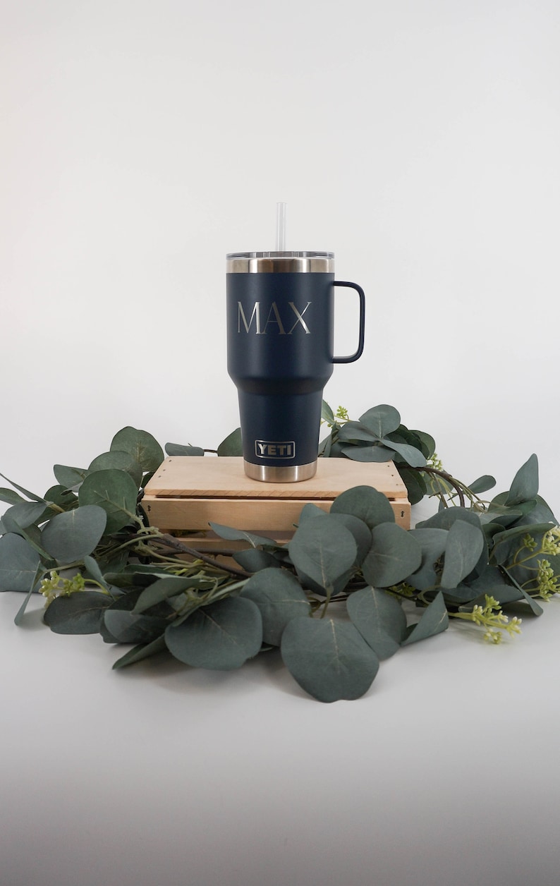 May include: A navy blue YETI tumbler with a straw and a handle. The tumbler has the name "MAX" engraved on the side.