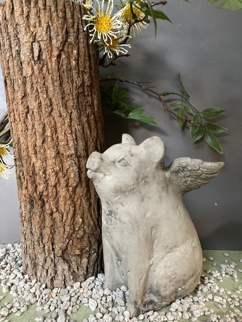 side profile of flying pig garden statue sitting on a green table displayed with various grey stones and a tree stump