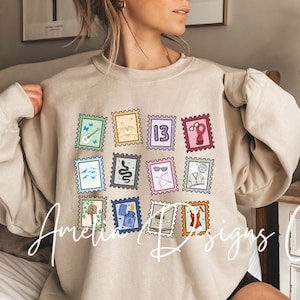 Puede incluir: Una sudadera de color arena con una cuadrícula de coloridos diseños de sellos postales. Cada sello muestra ilustraciones únicas, incluyendo una guitarra, un corazón y el número 13. La sudadera tiene mangas largas y un corte relajado.