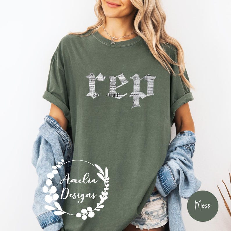 以下が含まれることがあります： 前面に白い文字で「REP」とプリントされた緑色のTシャツ。文字は新聞の印刷パターンで構成されています。シャツはデニムのショートパンツとデニムジャケットを着た人が着用しています。