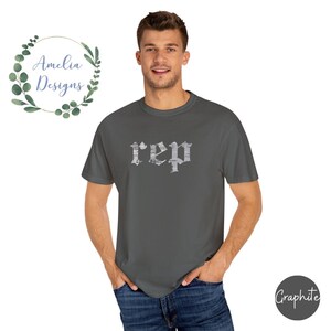 以下が含まれることがあります： グレーのTシャツに、白いかすれたフォントで「rep」とプリントされています。