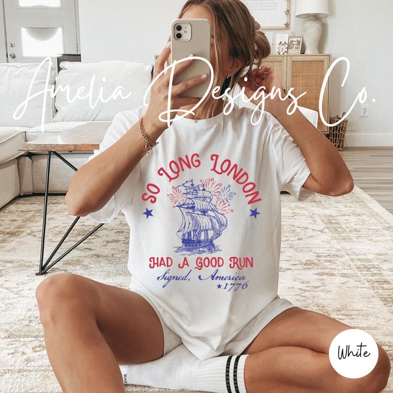 May include: White t-shirt with a patriotic design. The shirt features a blue and red illustration of a ship with fireworks, the text "So Long London, Had a Good Run, Signed, America, *1776".