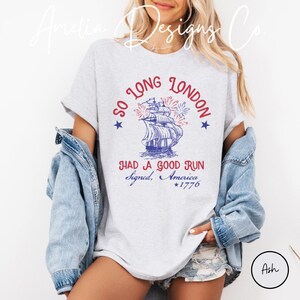 May include: Ash-colored t-shirt with a patriotic design. The graphic features a ship with fireworks, the text "SO LONG LONDON" and "HAD A GOOD RUN Signed, America *1776". The shirt is a casual wear item.