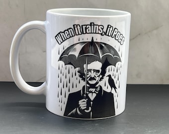 May include: White ceramic mug featuring a black and white illustration of Edgar Allan Poe under an umbrella in the rain, with a raven. The mug has the text "When it rains, it Poes".