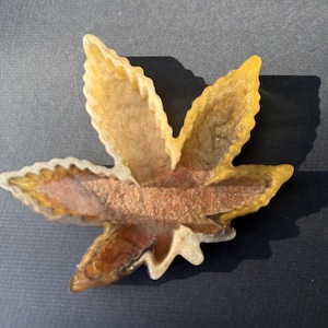 May include: A decorative, leaf-shaped resin tray with a gold and copper color scheme. The tray has a detailed, veined design and is set against a dark background. The tray is approximately 4 inches wide.