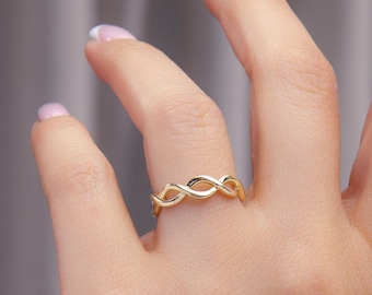 May include: A gold ring featuring a delicate, continuous twisted rope or infinity-style design. The band has a polished, smooth metallic finish and a slender profile that wraps around the finger in a repeating, symmetrical pattern of interlocking loops.