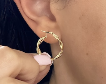 May include: A small, polished gold hoop earring featuring a distinct twisted, rope-like texture. The circular earring has a hinged closure mechanism and a reflective, metallic finish that catches the light, creating a bright, golden appearance.
