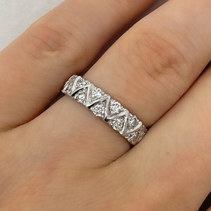 May include: A silver ring with a repeating geometric pattern of small, sparkling stones. The ring is on a finger with a light pink nail polish.
