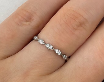 May include: A delicate silver band ring with a row of small, clear, marquise-shaped stones set in a scalloped design.