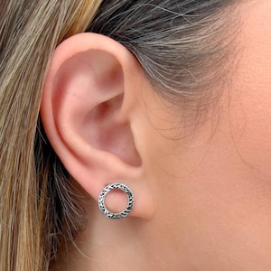 以下が含まれることがあります： テクスチャ加工された表面を持つ、銀色の円形のスタッドピアスのペア