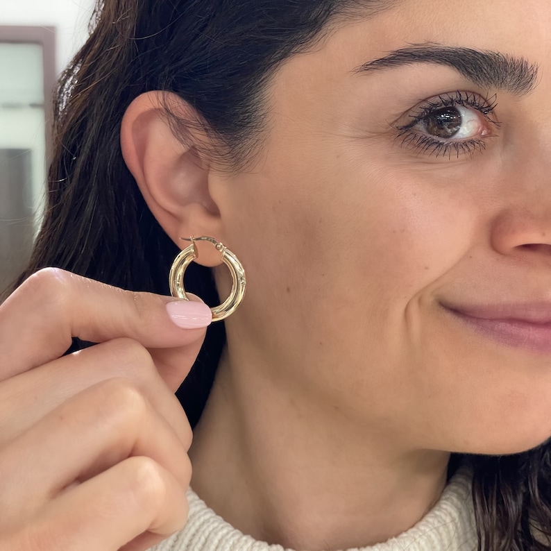 These 14k yellow gold round thick hoop earrings feature a rich, high polish shine, bringing out the tubular shape and smooth round finish. Click-top posts secure these trendy handcrafted yellow gold hoops, made for pierced ears. Lightweight hoops.