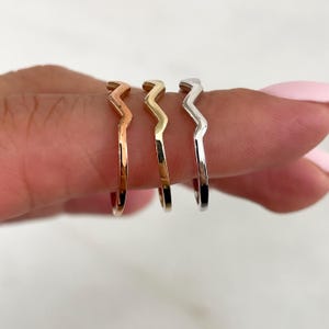 Pode incluir: Tr&ecirc;s an&eacute;is de metal finos com um topo distinto em forma de ziguezague ou chevron. O conjunto inclui um anel em tom de ouro rosa, um anel em tom de ouro amarelo e um anel em tom prateado, cada um com acabamento liso e polido.