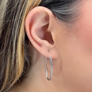 May include: Silver hammered hoop earrings. The earrings are oval shaped and have a textured finish.