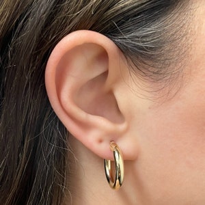 These 14k yellow gold round thick hoop earrings feature a rich, high polish shine, bringing out the tubular shape and smooth round finish. Click-top posts secure these trendy handcrafted yellow gold hoops, made for pierced ears. Lightweight hoops.