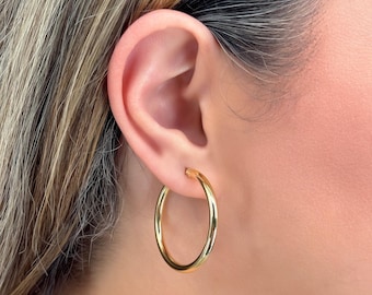 May include: Gold hoop earrings worn in a person's earlobe. The earrings are simple and classic.