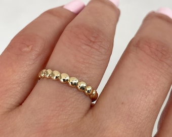 May include: A gold ring featuring a continuous band of small, polished, spherical beads arranged in a row. The metal has a bright, reflective finish, creating a uniform, textured appearance around the entire circumference of the circular jewelry piece.