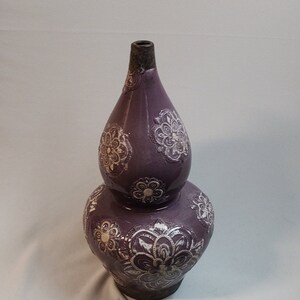 May include: A purple ceramic vase with a double gourd shape. The vase is decorated with white floral patterns.