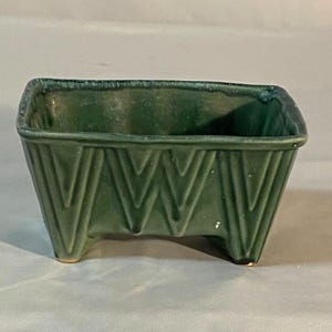 May include: A green ceramic planter with a geometric design and four legs. The planter is rectangular and has a glazed finish.