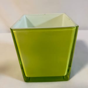 May include: A square, green glass vase with a white interior. The vase is made of clear glass with a green tint.