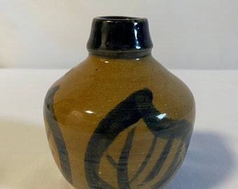May include: A small, brown ceramic vase with black abstract designs. The vase has a rounded body and a narrow neck.