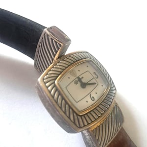 May include: A Brighton watch with a rectangular face and a brown leather band. The watch face is cream-colored with black hands and numerals. The watch has silver-toned metal accents and a black leather strap.