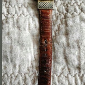 May include: A rectangular watch with a gold-tone bezel and a silver-tone band. The watch face is white with black numerals and hands. The brown leather strap shows wear. The watch is a classic accessory.
