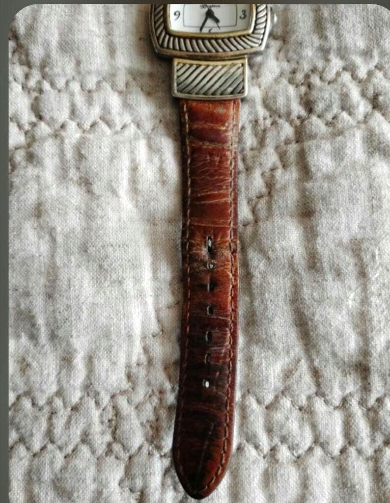 May include: A rectangular watch with a gold-tone bezel and a silver-tone band. The watch face is white with black numerals and hands. The brown leather strap shows wear. The watch is a classic accessory.