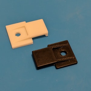May include: Two plastic clips, one white and one black, with a small hole in the center. The clips are designed to hold objects together.