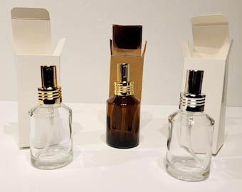 May include: Three glass spray bottles with different colored caps. The bottles are empty and sitting on a white surface. The bottles are in front of white boxes.