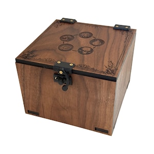 May include: A square wooden box with a dark brown finish, featuring a black metal latch and hinges. The lid is engraved with five circular symbols arranged in a pentagon pattern, surrounded by decorative corner filigree and a thin border.